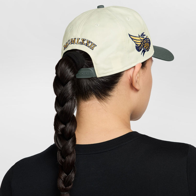 Sail snapback cap with dark green brim, winged emblem on back side; model wearing.