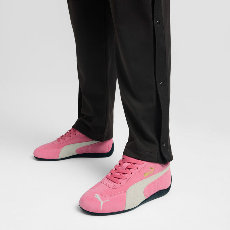 Youth pink Puma sneakers on feet with black pants; lace-up shoes with white side panel.