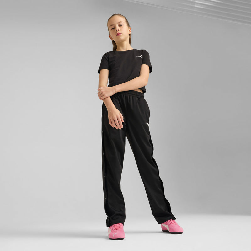 Youth model wearing pink Puma sneakers with black pants; lace-up shoes with black sole.
